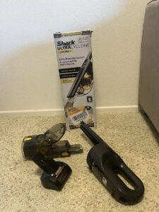 Cleaning embedded pet hair from car fabric upholstery using the Shark UltraCyclone Pet Pro+ handheld vacuum with its motorized pet brush attachment.