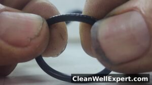 Close-up of black rubber O-ring seal from Shark vacuum dust cup being twisted between fingers revealing hidden cracks, flattening and displacement that cause air leaks