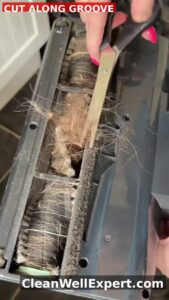 Close-up of hand using scissors to cut tangled hair and pet fur from Shark vacuum brush roll along designated cutting groove